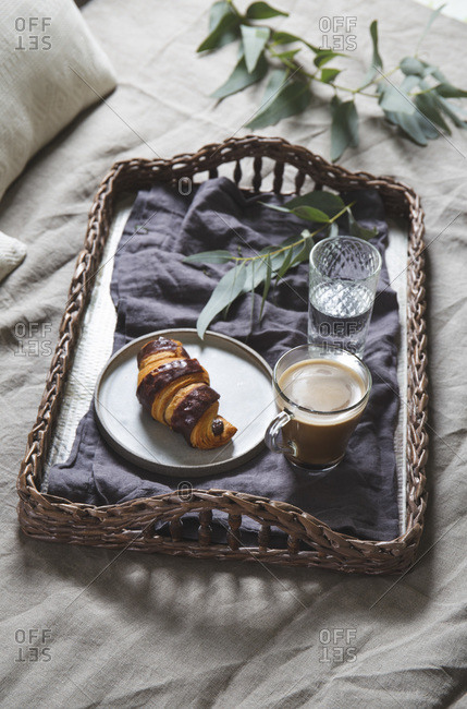 Wicker tray with coffee and croissant on a linen bed. Breakfast in bed.
