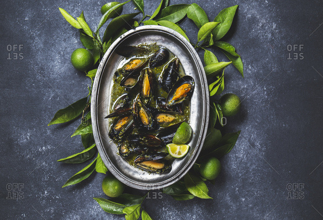 Mussels in green herb and white wine sauce with lemon on dark background.