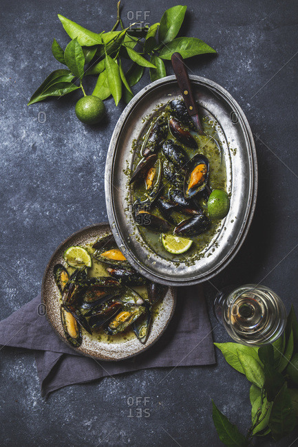 Mussels in green herb and white wine sauce with lemon on dark background.