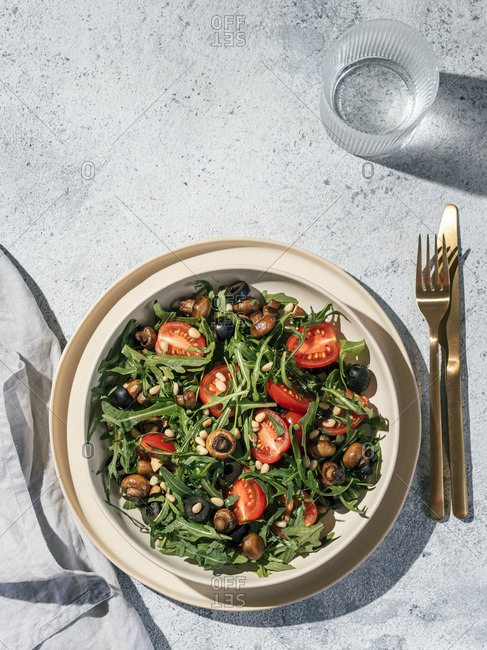 Salad with arugula, mini champignons, cherry tomatoes, black olives, pine nuts. Top view or flat lay. Copy space. Hard light. Vertical.