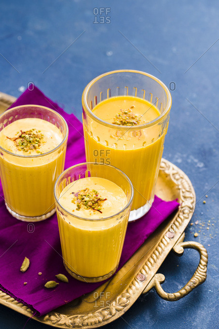 Three glasses of Mango Lassi garnished with saffron and crushed pistachio