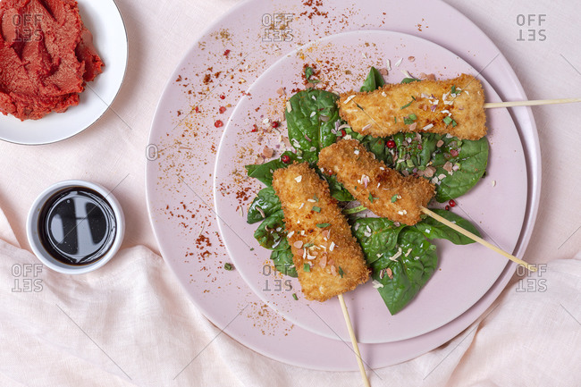 Chicken skewers in batter fried in fried panko on restaurant table with tomato concentrate, soy sauce, mustard sauce, spices and spinach Asian food