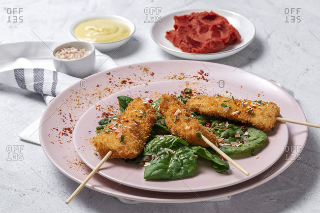 Chicken skewers in batter fried in fried panko on restaurant table with tomato concentrate, soy sauce, mustard sauce, spices and spinach Asian food