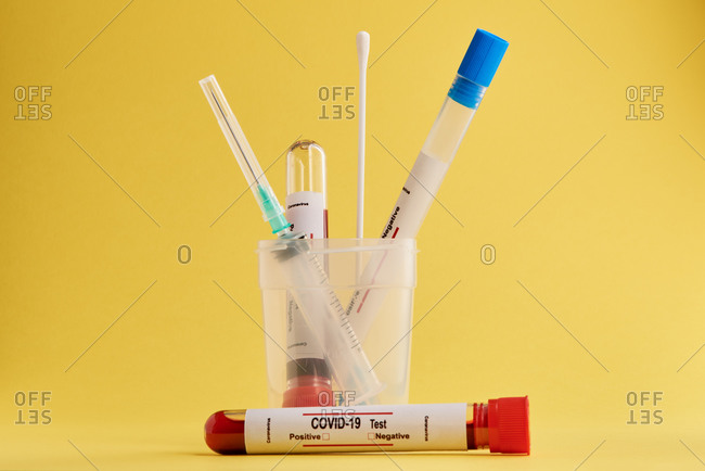Test tubes with blood samples and cotton swabs for nasal or saliva swab used for COVID 19 diagnostic on yellow background