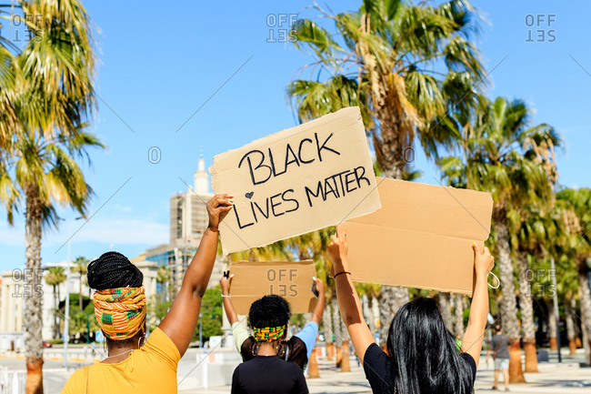 Back view of ethnic female with afro hairstyle holding cardboard poster with black lives matter inscription during demonstration at beach