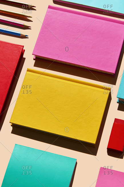 high angle view of some notebooks, erasers and pencils of different colors on a pale pink background