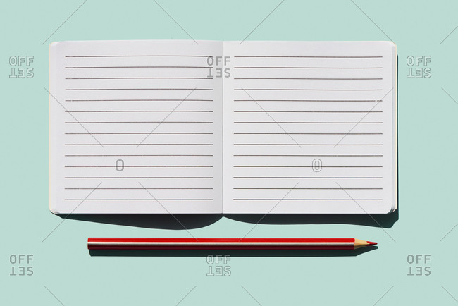high angle view of a red pencil and a blank lined paper notebook open on a blue background