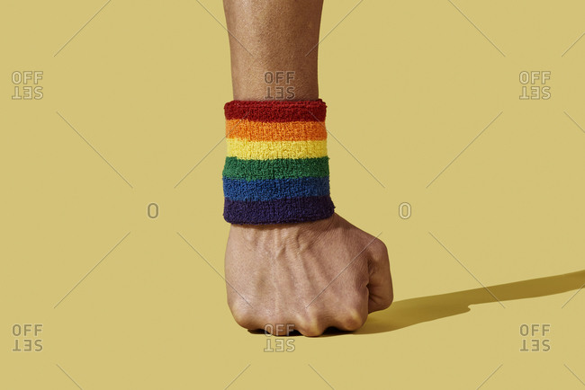 closeup of the arm of a young person wearing a rainbow-patterned wristband on a yellow background