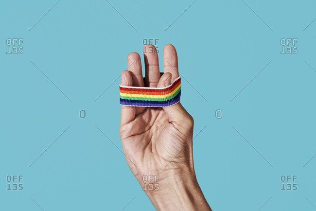 closeup of a young person with a rainbow-patterned wristband in his hand on a blue background