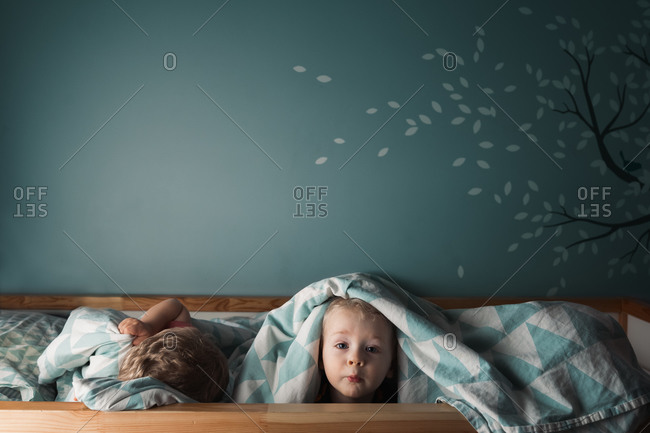Little boys in bed with one peaking out from under the blanket