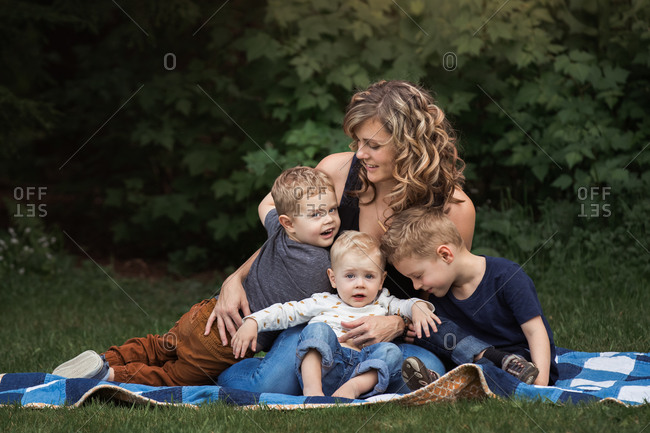 Woman holding three sons on a blanket outdoors