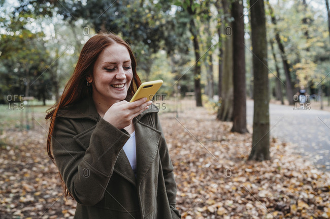 Young woman with long red hair taking smartphone selfie in autumn park