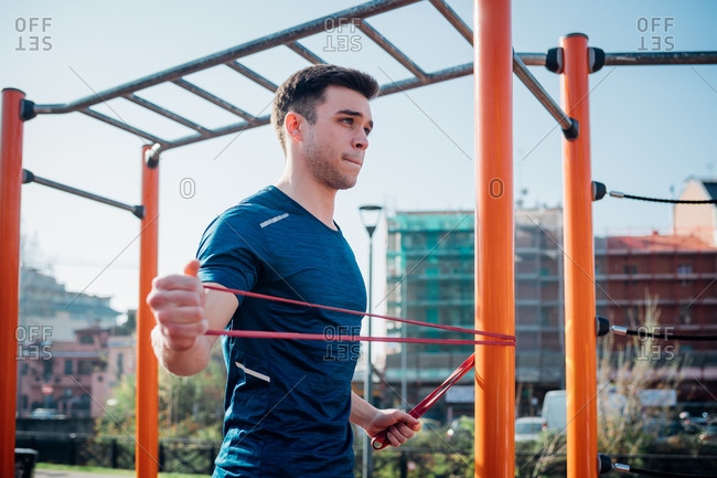 Calisthenics at outdoor gym, young man stretching arms on exercise equipment