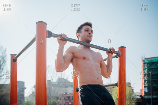 Calisthenics at outdoor gym, bare chested young man doing pull up on exercise equipment
