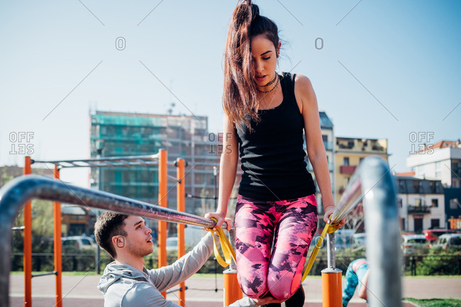 Calisthenics class at outdoor gym, male trainer encouraging young woman on parallel bars
