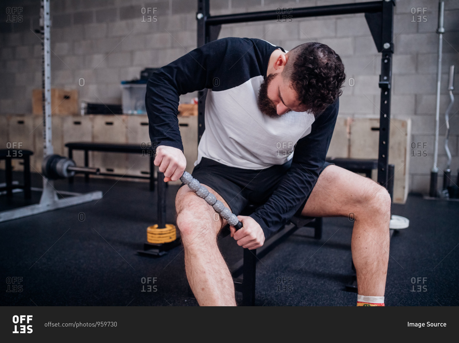 Young man massaging thigh with muscle roller stick in gym