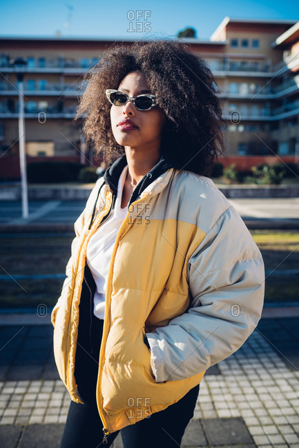 Cool young woman wearing sunglasses on urban sidewalk, three quarter length portrait