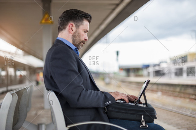 Side view of confident mature businessman working on digital tablet while waiting at railroad station
