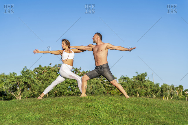Mature couple doing yoga on lawn in sunshine together