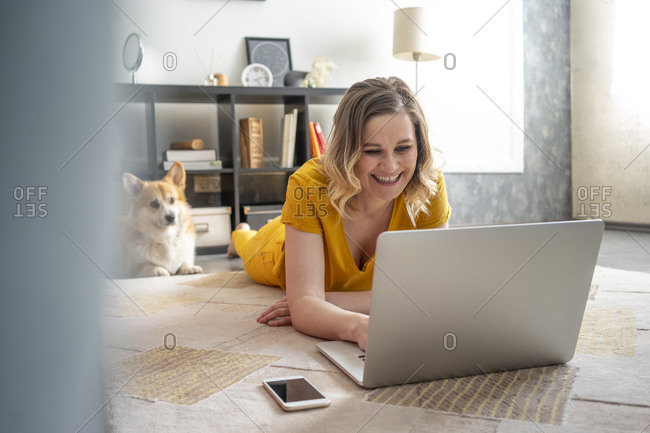 Happy woman with dog using laptop in living room at home