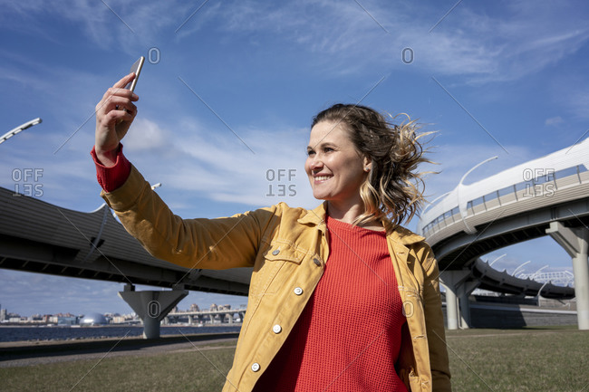 Happy woman with windswept hair taking a selfie at a road bridge