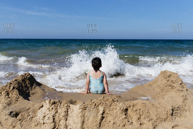 Back view of little girl in panties jumping into sea waves while