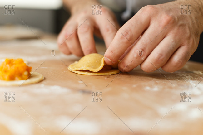 Faceless cook pressing edges of pumpkin ravioli with fingers on table while preparing gourmet dish in cozy home kitchen in daylight