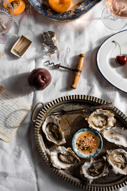 Oysters in a rustic dish on table with white cloth and fruit