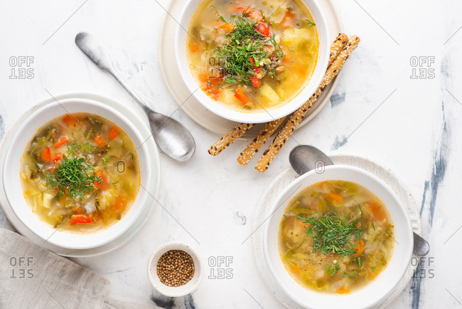 Vegetable soup served in white bowls with bread sticks on white background