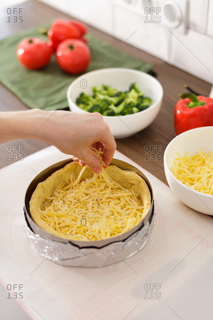 Woman placing cheese into quiche crust for recipe in kitchen