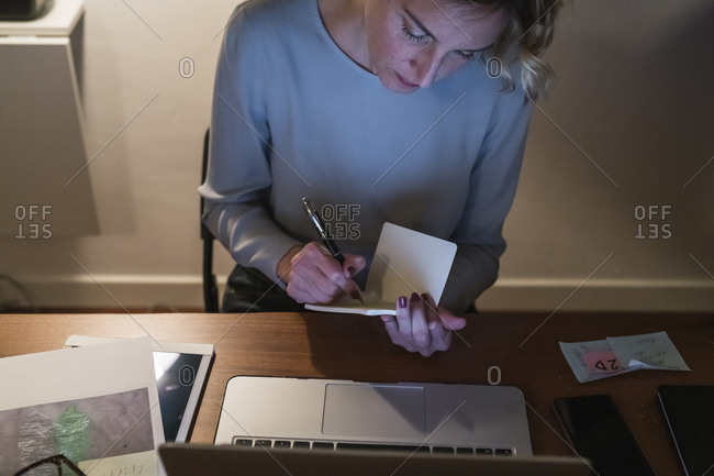 Woman at laptop, writing in notebook