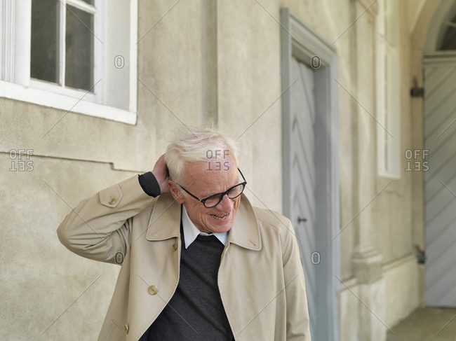 Senior man in raincoat scratching his head, Copenhagen, Hovedstaden, Denmark