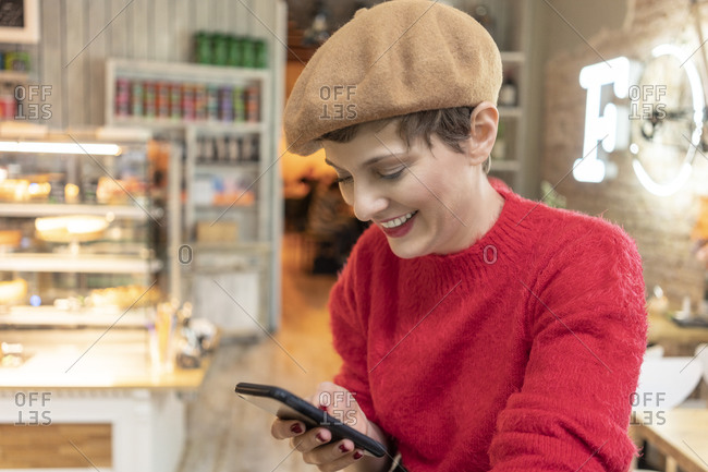 Mid adult woman in beret, looking at smartphone in cafe