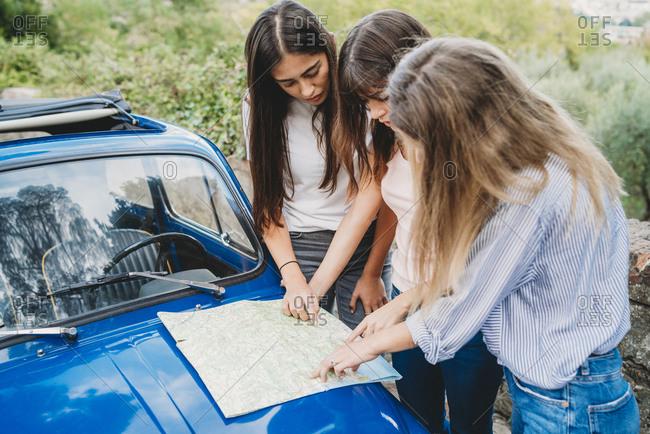 Friends reading route map on car bonnet in countryside