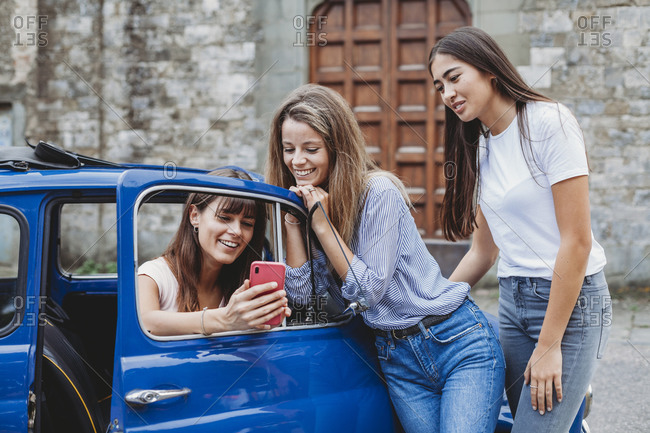 Friends using smartphone beside car