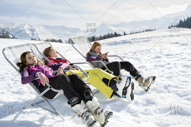 Three teenage girl skiers sitting in deck chairs in snow covered landscape, Tyrol, Styria, Austria