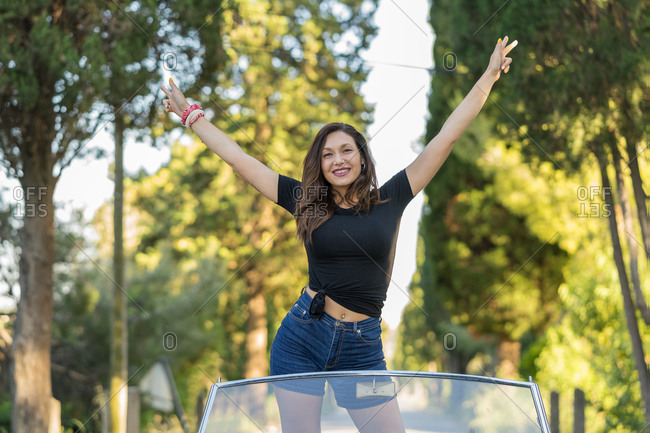 Beautiful and happy woman inside a cabriolet car raising arms and smiling