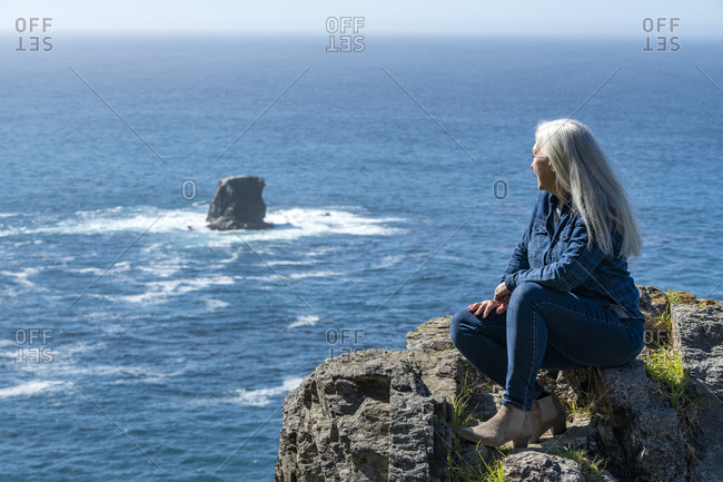 USA, California, Big Sur, Woman sitting at the edge of cliff looking at view