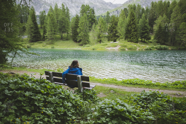 Switzerland, Bravuogn, Palpuognasee, Young woman resting on bench near Palpuognasee lake in Swiss Alps