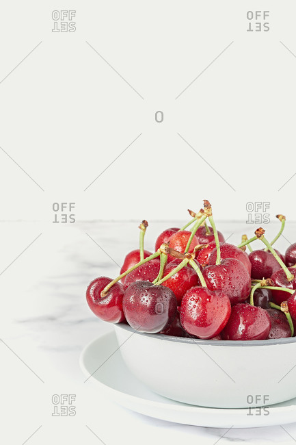 Fresh ripe red cherry with stalks in white ceramic pot placed on marble table against white wall