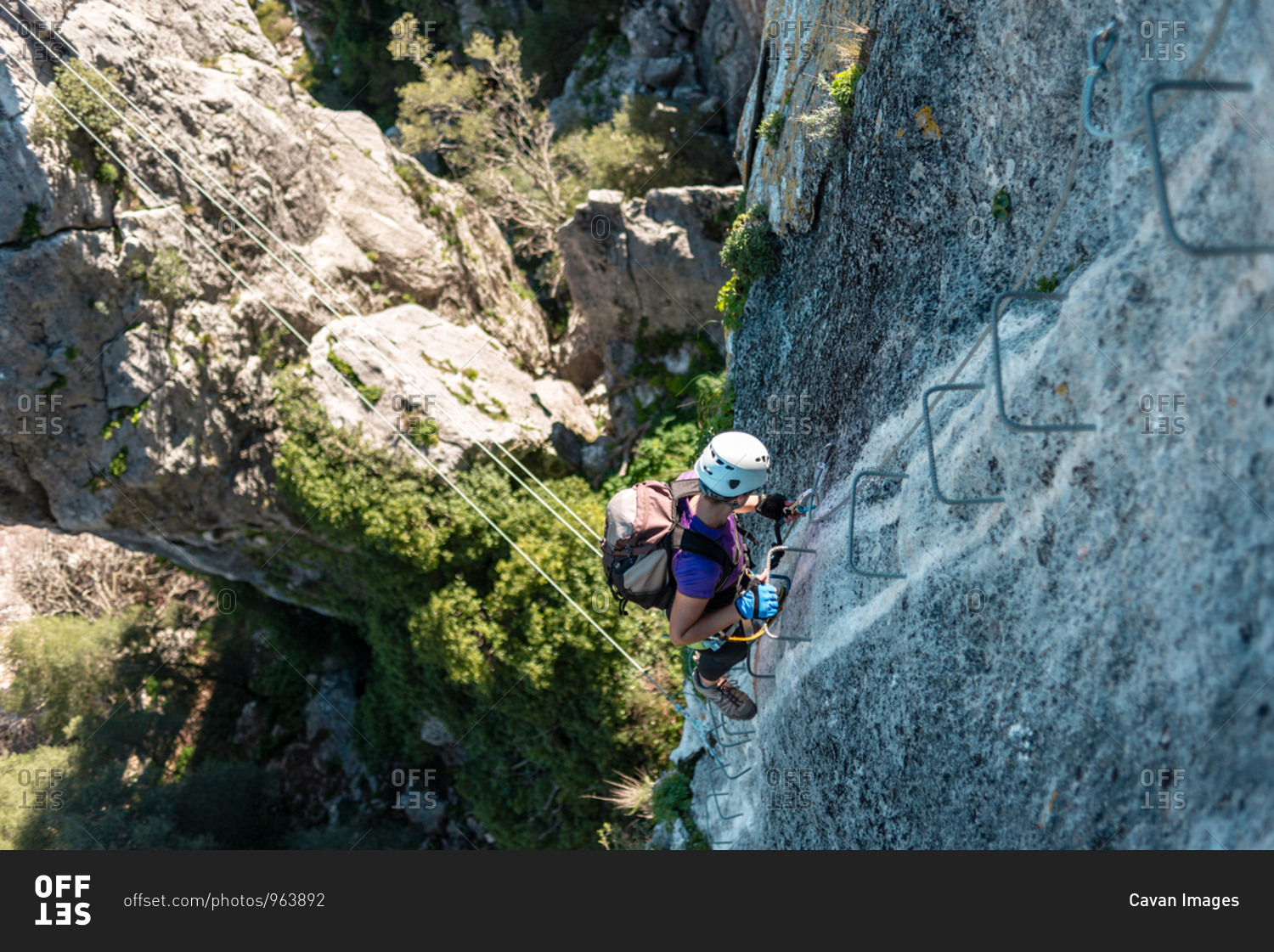 Woman with helmet, harness and backpack walking down via ferrata in the mountains.