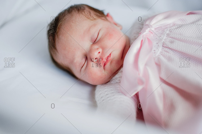 High angle of adorable baby girl in cozy dress lying in cot while sleeping