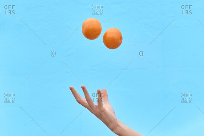 Crop woman tossing fresh orange in air showing concept of healthy diet on blue background