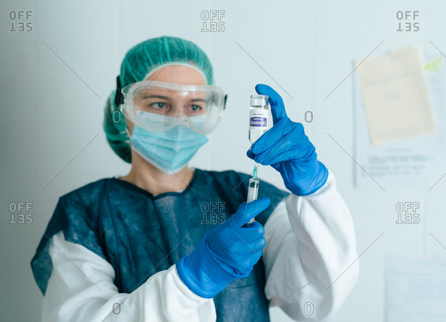 Young female medical specialist in protective mask and gloves  filing syringe with vaccine from vial for prevention and immunization from coronavirus infection