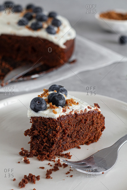 Slice of homemade chocolate sponge cake topped with fresh whipped cream and whole blueberries placed on table in light kitchen