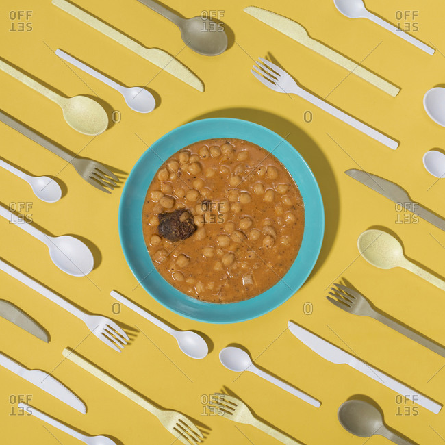 Top view of minimal composition of Callos with a bunch cutlery over yellow background