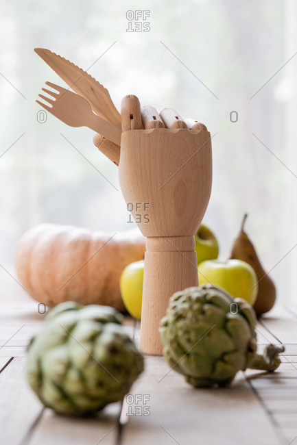 Wooden hand with knife and fork placed on table with fresh fruits and vegetables for nutritious diet