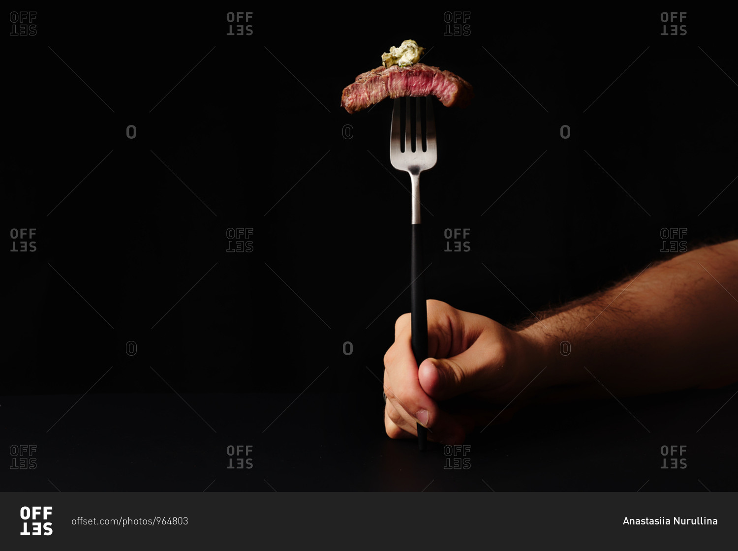 Male hand holding a fork with a slice of beef medium rare steak served with herb butter on it
