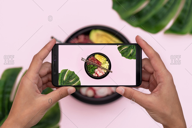 Top view of woman taking picture of tuna poke bowl on pink background