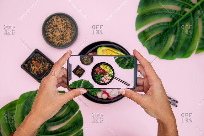 Top view of woman taking picture of tuna poke bowl on pink background
